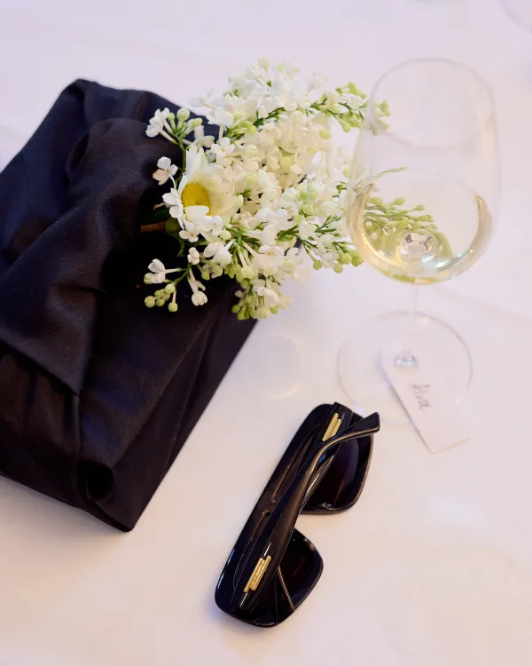 An Orrefors gift wrapped in a black fabric decorated with fresh flowers and, next to the gift, a cava glass and sunglasses