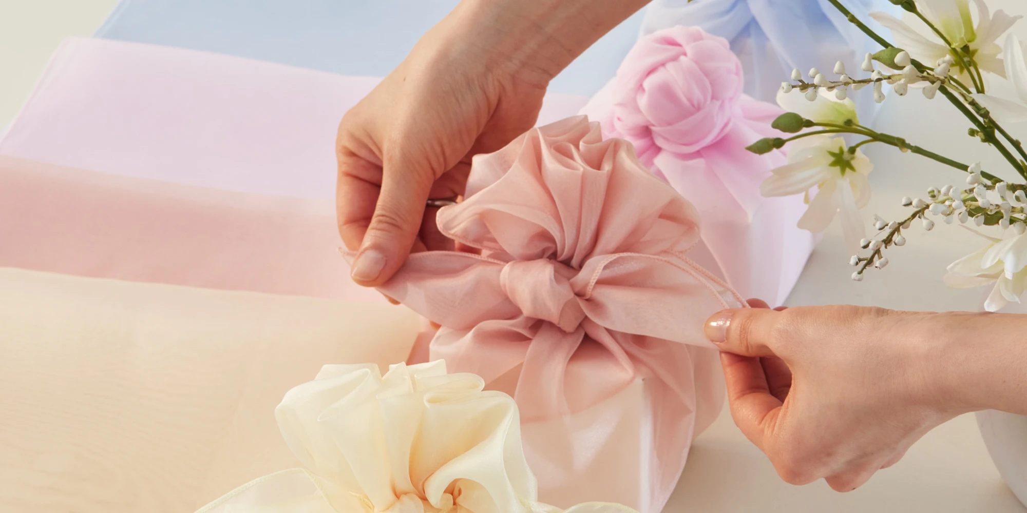 Several gifts, each uniquely wrapped in different colors, and a person adding final touches to one.