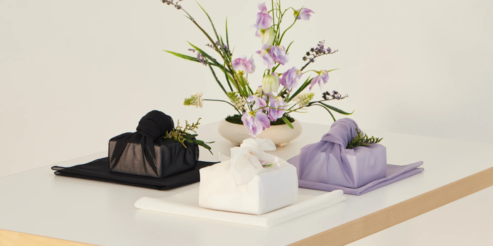 Three luxury corporate gifts wrapped in premium fabrics in different colors, styled on a presentation table