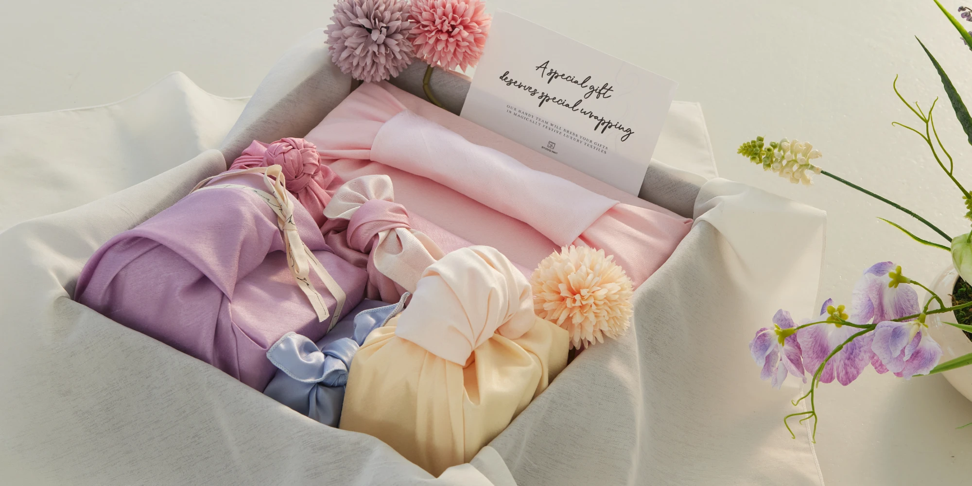 Multi-gifts of various-size, elegantly wrapped in premium textiles and diverse designs, all neatly enclosed within a larger box